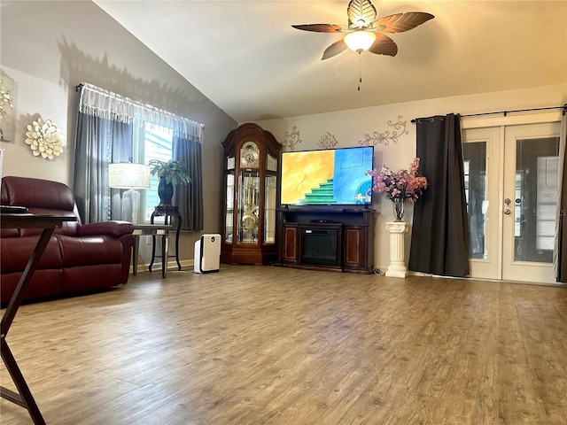 living area with a ceiling fan, wood finished floors, vaulted ceiling, french doors, and a fireplace