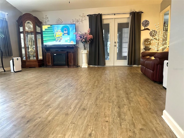 living area featuring french doors, a fireplace, baseboards, and wood finished floors