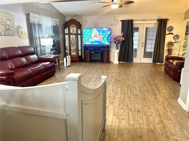 living area with ceiling fan, a fireplace, wood finished floors, vaulted ceiling, and french doors