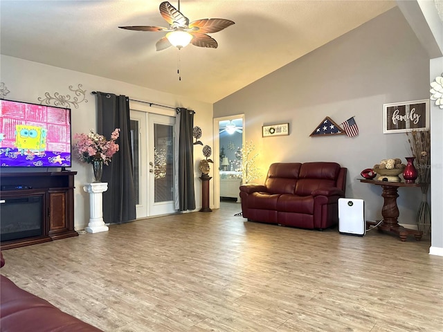 living room with baseboards, a ceiling fan, a glass covered fireplace, lofted ceiling, and wood finished floors