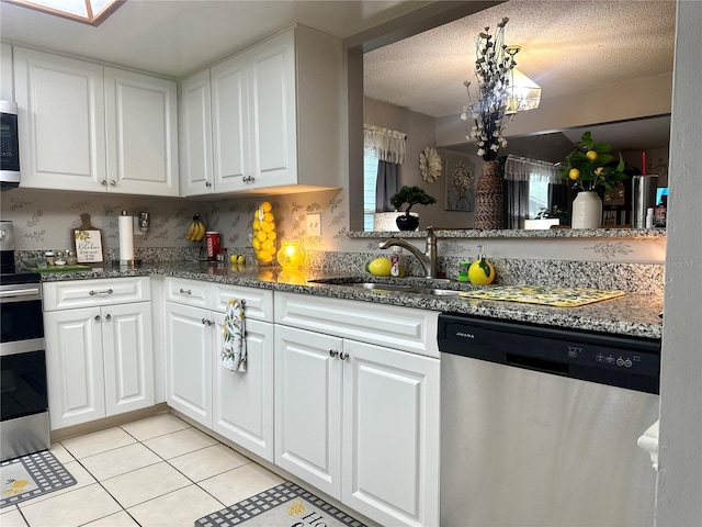 kitchen with decorative backsplash, appliances with stainless steel finishes, white cabinetry, a sink, and light tile patterned flooring