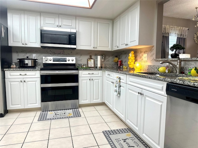 kitchen featuring light tile patterned floors, stainless steel appliances, backsplash, white cabinetry, and a sink