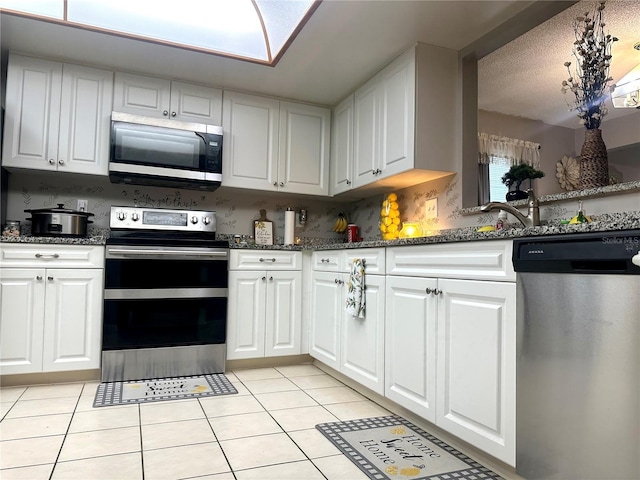 kitchen with appliances with stainless steel finishes, light tile patterned flooring, and white cabinets