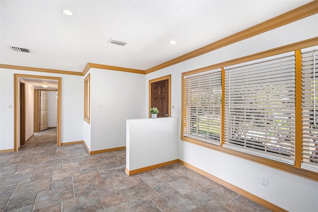 unfurnished room featuring crown molding, stone finish flooring, visible vents, and baseboards