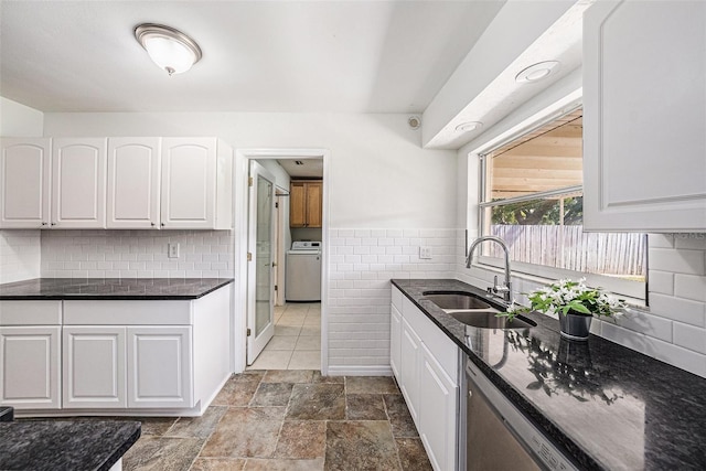 kitchen with a sink, white cabinetry, stainless steel dishwasher, dark stone counters, and washer / dryer