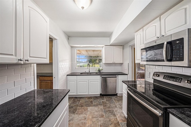 kitchen with stainless steel appliances, backsplash, white cabinets, a sink, and dark stone counters