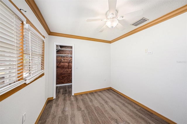 spare room featuring ornamental molding, visible vents, baseboards, and wood finished floors