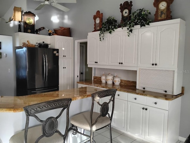 kitchen featuring light tile patterned flooring, stone counters, white cabinetry, and freestanding refrigerator