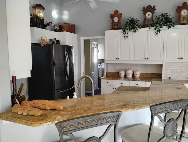 kitchen featuring light stone counters, a kitchen breakfast bar, freestanding refrigerator, white cabinetry, and a sink