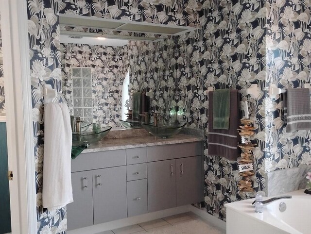 full bath with a garden tub, double vanity, wallpapered walls, a sink, and tile patterned floors