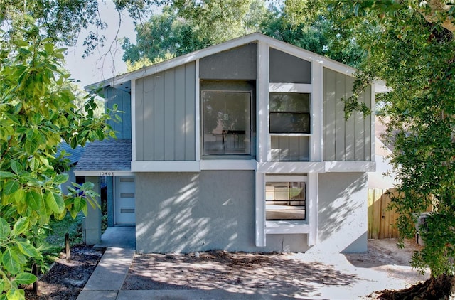 view of front of property featuring board and batten siding, roof with shingles, fence, and stucco siding