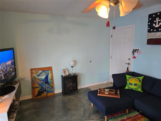 living area featuring a wood stove, finished concrete flooring, baseboards, and a ceiling fan