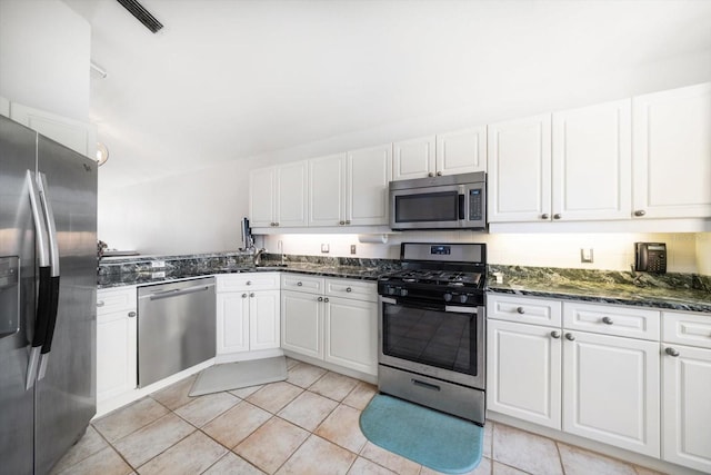 kitchen featuring appliances with stainless steel finishes, white cabinetry, a sink, and dark stone countertops