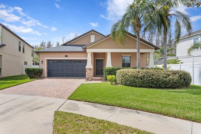 craftsman-style house with a garage, fence, decorative driveway, stucco siding, and a front lawn