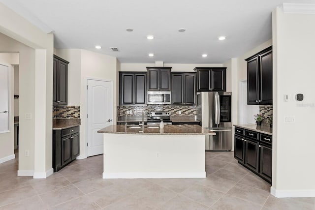 kitchen with stone countertops, visible vents, an island with sink, stainless steel appliances, and a sink