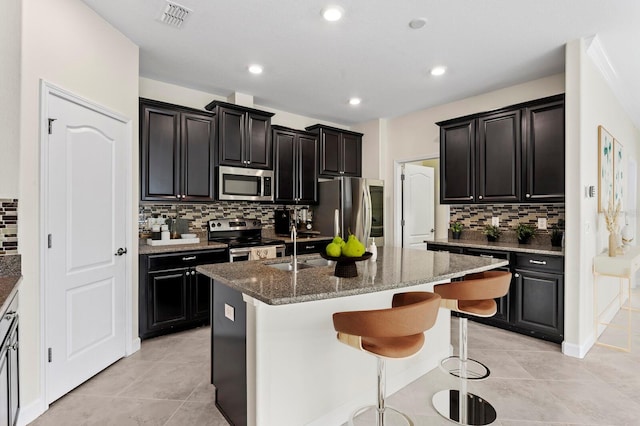 kitchen with a center island with sink, stainless steel appliances, visible vents, light tile patterned flooring, and dark stone counters