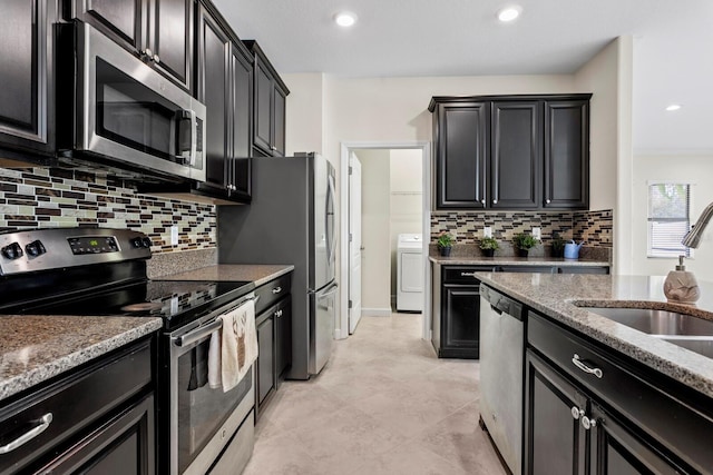 kitchen featuring light stone counters, stainless steel appliances, decorative backsplash, washer / dryer, and dark cabinetry