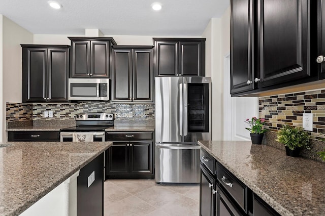 kitchen featuring dark stone counters, stainless steel appliances, backsplash, and dark cabinets