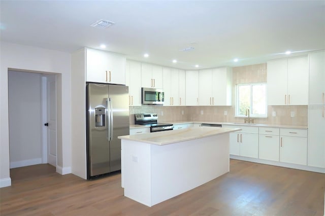 kitchen featuring stainless steel appliances, wood finished floors, backsplash, and a sink