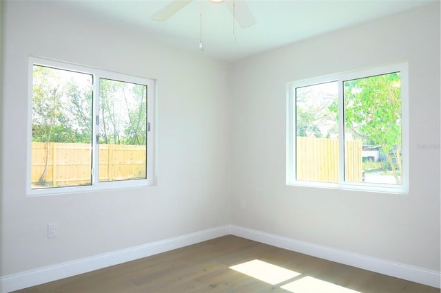 spare room featuring plenty of natural light, wood finished floors, a ceiling fan, and baseboards