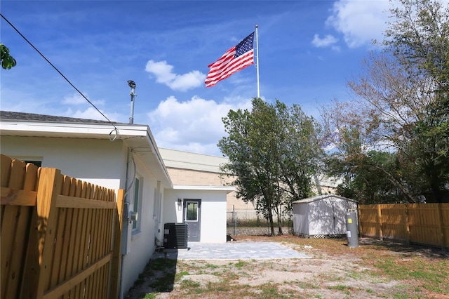 exterior space featuring stucco siding, central AC, a shed, a fenced backyard, and an outdoor structure