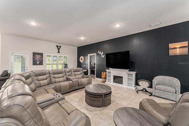 living room featuring light tile patterned floors, recessed lighting, an accent wall, visible vents, and a glass covered fireplace