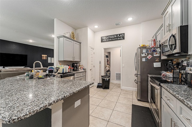 kitchen featuring light tile patterned floors, a textured ceiling, stainless steel appliances, open floor plan, and dark stone countertops