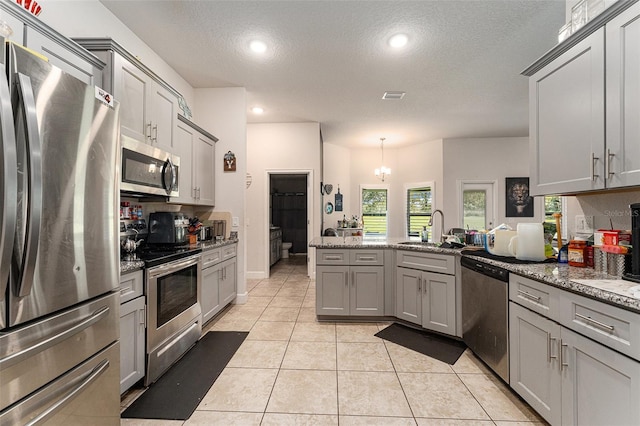 kitchen with a sink, stainless steel appliances, a peninsula, and gray cabinets