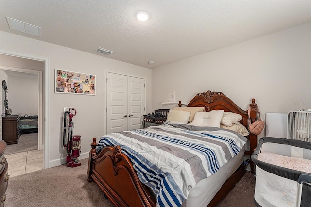 bedroom with a textured ceiling, light carpet, visible vents, baseboards, and a closet