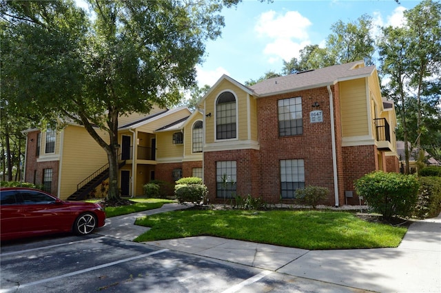 view of property featuring a front lawn, stairway, uncovered parking, and brick siding