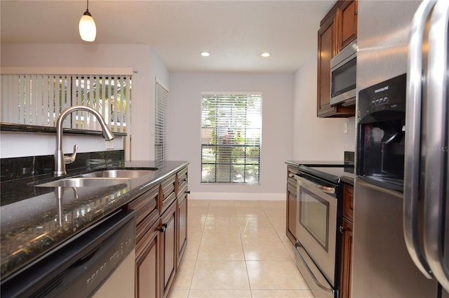 kitchen featuring a sink, dark stone counters, appliances with stainless steel finishes, light tile patterned flooring, and baseboards