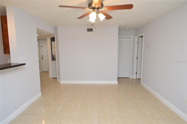 empty room featuring light tile patterned floors, baseboards, visible vents, and ceiling fan