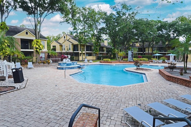 view of swimming pool featuring a patio area, a residential view, a pool with connected hot tub, and fence