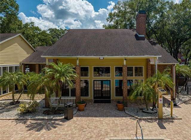 back of property featuring french doors, a chimney, and a shingled roof