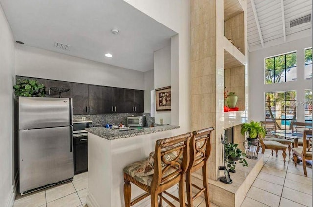 kitchen featuring light tile patterned floors, visible vents, a toaster, appliances with stainless steel finishes, and a towering ceiling
