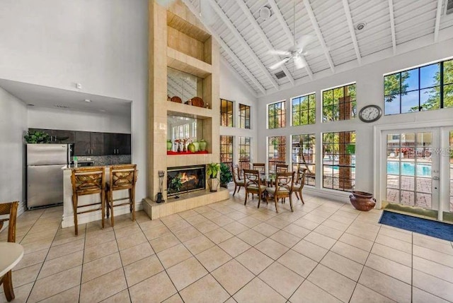 sunroom featuring a tile fireplace, wood ceiling, lofted ceiling with beams, and a ceiling fan
