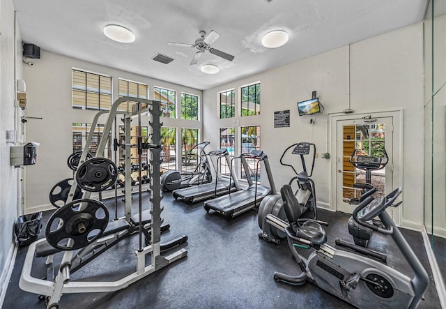 exercise room with visible vents, baseboards, ceiling fan, and a towering ceiling