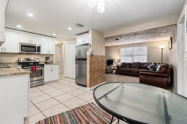 kitchen featuring light tile patterned floors, visible vents, white cabinets, open floor plan, and stainless steel appliances