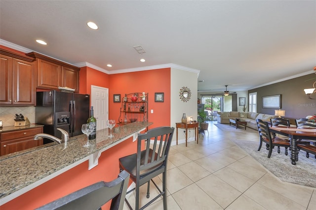 kitchen featuring light stone counters, black fridge with ice dispenser, a kitchen breakfast bar, open floor plan, and decorative backsplash