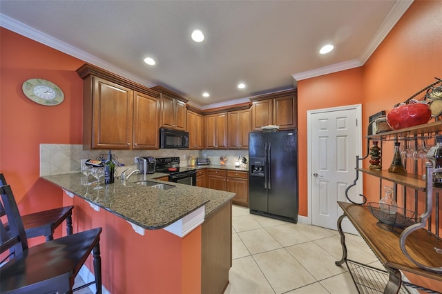 kitchen with a peninsula, a sink, ornamental molding, black appliances, and dark stone countertops