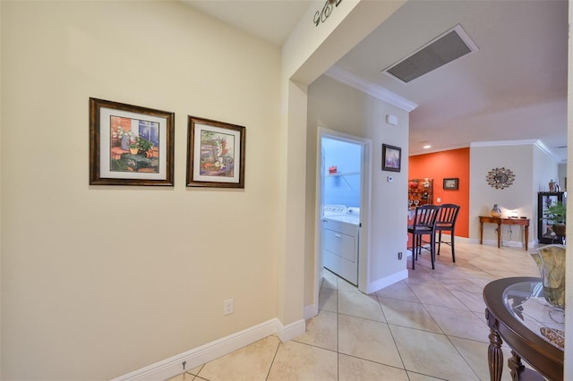 hall featuring light tile patterned floors, visible vents, ornamental molding, washer / dryer, and baseboards