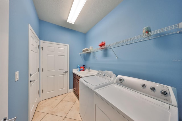 washroom with light tile patterned floors, cabinet space, a sink, a textured ceiling, and washer and dryer