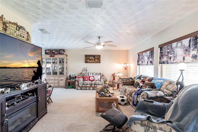 living room with light carpet, a textured ceiling, visible vents, and a ceiling fan