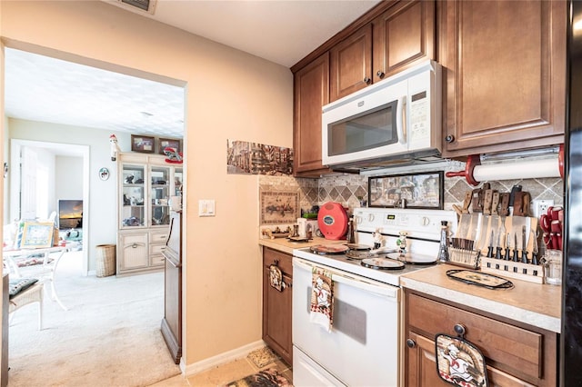 kitchen with light countertops, backsplash, light carpet, white appliances, and baseboards