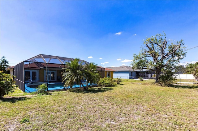 rear view of house with glass enclosure, a lawn, fence, and an outdoor pool