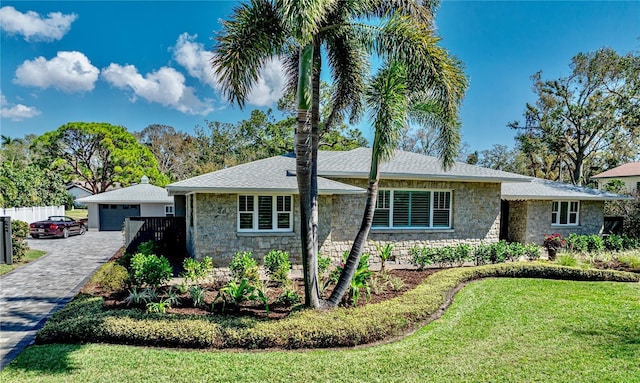 ranch-style house featuring an outbuilding, a detached garage, fence, stone siding, and a front lawn