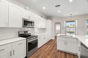 kitchen with dark wood-style floors, arched walkways, light countertops, appliances with stainless steel finishes, and white cabinetry