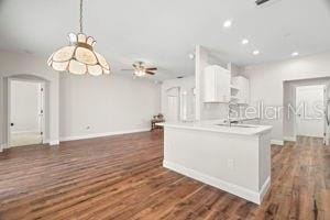 kitchen with arched walkways, dark wood finished floors, recessed lighting, light countertops, and hanging light fixtures