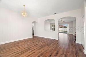 spare room featuring baseboards, arched walkways, wood finished floors, and ceiling fan with notable chandelier