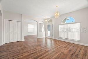 spare room featuring arched walkways, a notable chandelier, wood finished floors, and baseboards